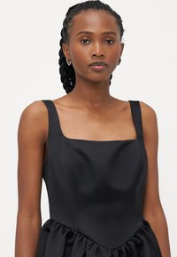 Melnas satīna kleitas ar kvadrātveida izgriezumu, biezām plecu siksnām un savītu svārku. Gluda tekstūra ar elegantu dizainu, kas piedāvā minimālisma akcentus.