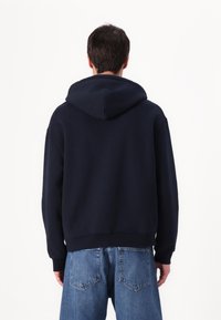 Felpa blu navy con un ampio cappuccio regolabile, spalle scese e orli a coste; abbinata a jeans in denim azzurro.