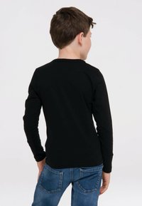 Schwarzes Langarmshirt aus Baumwolle mit Rundhalsausschnitt und taillierten Ärmeln, getragen mit blauen Jeans und von hinten gezeigt.