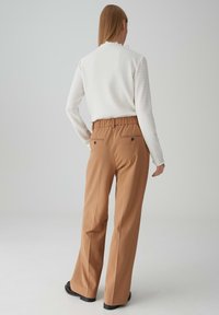 Bordeauxkleurige wijde broek met een elastische tailleband en twee achterzakken. Draagt een gestructureerd wit longsleeve shirt.