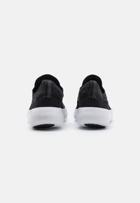 Zapatillas deportivas de punto negras con una suela blanca, que cuentan con una parte superior texturizada, un cuello acolchado y una lengüeta en el talón para facilitar su colocación.