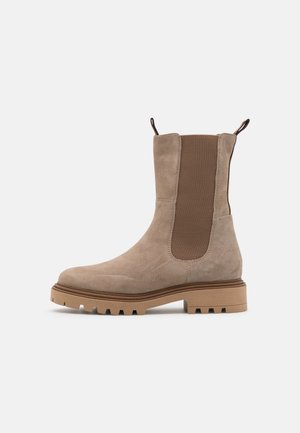 Bottine Chelsea mi-haute en daim beige avec panneau latéral élastique, languettes, semelle en caoutchouc épaisse et motif de semelle rugueux.