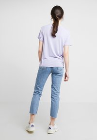 Fialové tričko s krátkým rukávem, měkká látka, volný střih, spárované se světle modrými džínami s vysokým pasem, zkrácené nohavice a bílé tenisky.