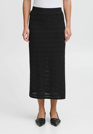 Gonna midi nera in maglia con un design strutturato, caratterizzata da strisce orizzontali e una vita attillata. Abbinata a scarpe nere con punta.