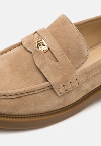Beige suede instapschoenen met een goudkleurig logoaccent. Beschikt over een ronde neus, gestikte details en een dikke rubberen zool.
