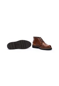 Bottines en cuir marron avec un bout rond, un laçage, des coutures décoratives et des semelles en caoutchouc noir texturé. Une bottine est présentée debout, l'autre à plat.