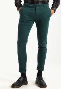 Gröna manchesterbyxor med smal passform, med upprullade fållar och knappstängning fram. Kombinerat med svarta snörskor.