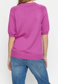 Pull en maille fuchsia avec manches courtes bouffantes et ourlet côtelé, présentant une texture lisse et un design décontracté, porté avec un jean clair.