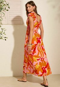 Blumenmaxikleid mit pinkem Grund, das große orangefarbene und gelbe Blattmuster zeigt, mit einem gerafften Bund und kurzen, volantringartigen Ärmeln.
