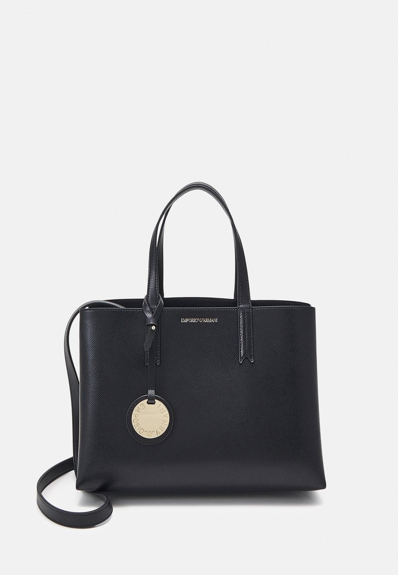 Czarna torebka z teksturowanej skóry z dwoma uchwytami, paskiem na ramię oraz okrągłą złotą metką z logo zawieszoną z przodu.
