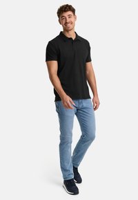 Camisa polo negra de manga corta con collar, combinada con Jeans de mezclilla azul claro y zapatillas oscuras. Tela suave con corte ajustado.