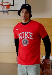 Punane Nike t-särk mustade pikkade varrukatega, millel on "NIKE" ja "CHICAGO BULLS" graafika; kombineeritud heledate siniste teksade ja musta ämbrihatu ka.