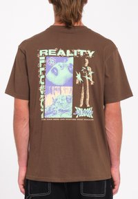 Camiseta gráfica de algodón marrón con texto en negrita, imágenes multicolores y un corte relajado. El diseño incluye elementos visuales como estrellas y rostros.