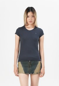 T-shirt aderente blu navy in morbido tessuto con maniche corte e scollatura rotonda. Abbinato a una gonna di jeans a fantasia con blocchi di colore.