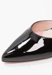 Chaussure plate en cuir verni noir à bout pointu, avec une surface lisse et brillante et une doublure intérieure beige clair.