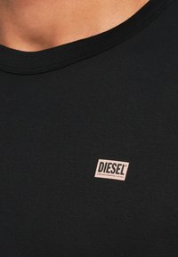 Fekete rövid ujjú póló kerek nyakkivágással, a mellrészen egy kis rózsaszín Diesel logóval hímzett címkével. Sima, puha anyag.