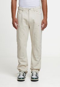 Beeži toonitud p üksid esitaskutega, hõbedase värvikaunistusega ja lõdva istuvusega, millega on kombineeritud roheliste aktsentidega tossud ja valge tankitopp.