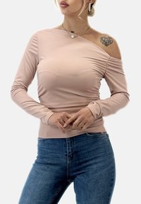 Ljusrosa långärmad topp med ensidig axeldesign, med en slät textur och veckad detalj vid sidan. Matchas med blå högmidjade jeans.