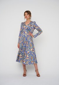 Bloemmotief blauwe jurk met lange mouwen, V-hals en een vloeiende silhouet, benadrukt door oranje en witte bloemen en paisley-details.