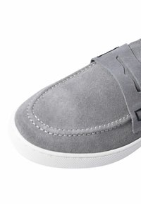Scarpa slip-on in suede grigio con suola in gomma bianca, dotata di accenti cuciti e una finitura testurizzata, con un design a punta arrotondata.