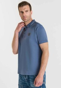 Polo shirt blu con colletto, tre bottoni e una sottile rifinitura bianca sul colletto. Il tessuto sembra liscio con un design aderente.