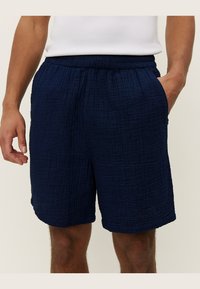 Pantaloni scurți de culoare albastru marin, realizați dintr-un material texturat cu un model matlasat, având o talie elastică și buzunare laterale.