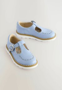 Zapatos de cuero azul claro con patrones de estrellas recortados, una correa con hebilla y suelas texturizadas blancas; cuentan con una plantilla floral.
