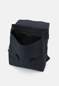 Sac bleu foncé avec une texture lisse, ouverture en haut et doubles bretelles. Dispose d'un intérieur spacieux avec un design simple et minimaliste.