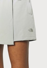 Ljust grå skorts i mjukt material, med rak skärning, synliga sömmar och en logotyp på nedersta högra sidan.