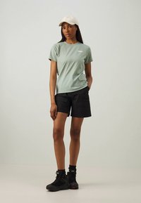 Hele roheline lühikeste varrukatega t-särk küljetaskuga, mida on kombineeritud mustade cargo-pükste ja mustade matkasaabastega ning millel on beež nokamüts.