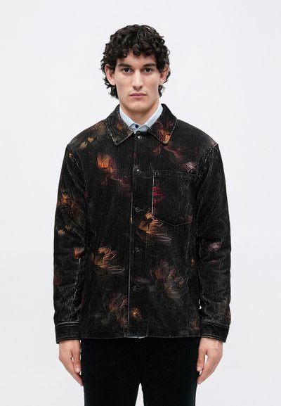 Veste en velours côtelé noir avec un motif floral dans des tons chauds. Elle possède une fermeture à boutons, une poche poitrine et des manches longues avec des ourlets à poignets.