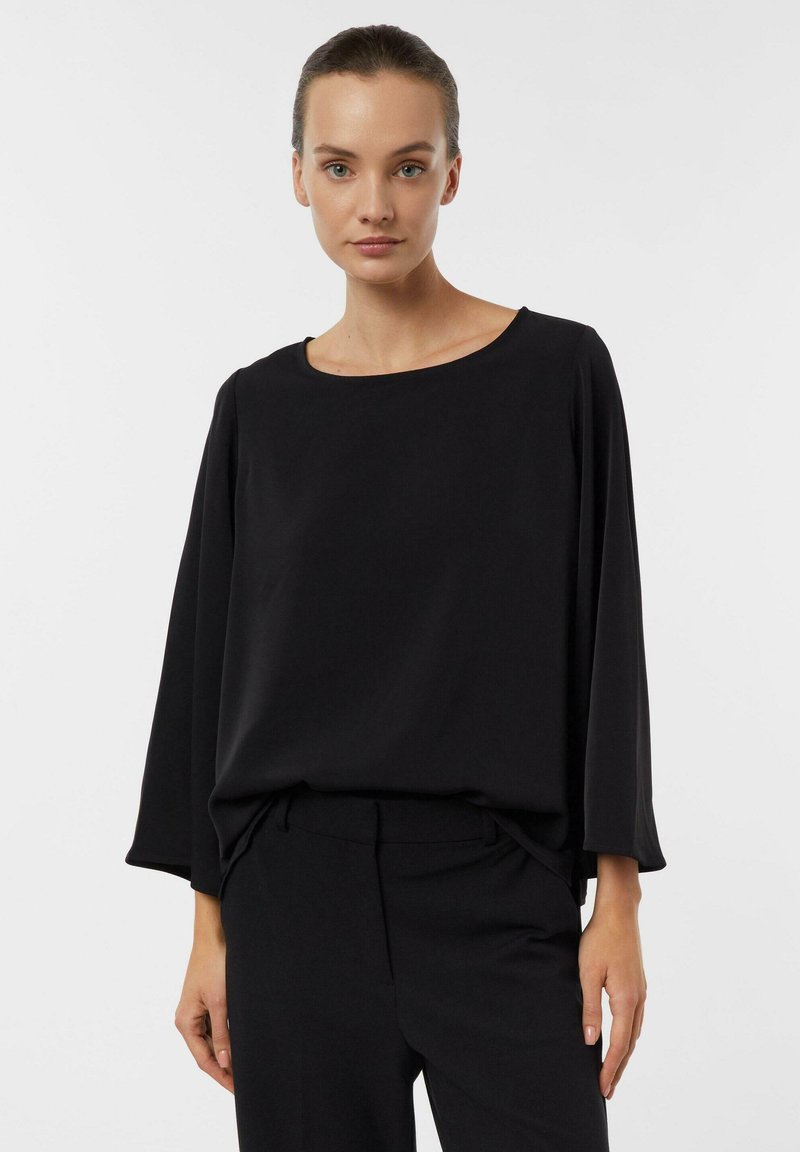 Schwarzes langärmeliges Oberteil mit rundem Ausschnitt, lockerem Schnitt und glatter Textur, kombiniert mit passenden schwarzen Hosen, minimalistisches Design.