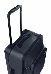 Borsone con ruote in tessuto nero, dotato di manico retrattile e due cerniere frontali. Superficie strutturata con cuciture robuste e dettagli.