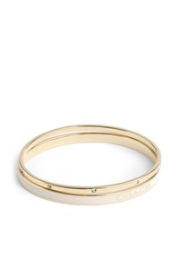 Pulsera de bangle en tono dorado que presenta un diseño de metal liso con una sección de esmalte blanco y pequeños acentos de cristal claro. Detalle del logotipo grabado.