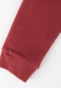 Bordeauxfarbene Baumwoll-Sweatpants mit weicher Textur, schmal zulaufendem Bein und gerippten Bündchen für einen engen Sitz. Einfaches Design ohne zusätzliche Akzente.