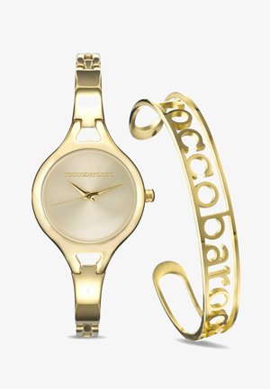 Zlatý hodinky s kulatým pouzdrem a minimalistickým ciferníkem, doplněné zlatým náramkem s vyřezávaným písmenkovým designem.