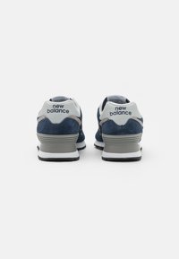 Sinised sametist tennisetossud, millel on valge nahkne konts, hallid aksendid ja must kummitald. Kontsal on nähtav "New Balance" logo.