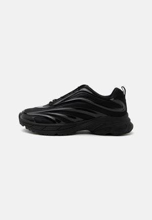 Czarny sportowy sneaker z błyszczącymi, falistymi nakładkami, wyściełaną podeszwą i pętelką na pięcie, pokazany z profilu na białym tle.