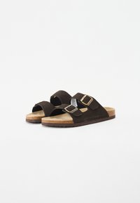 Sandales en daim marron avec deux boucles réglables, semelle en liège et semelle en caoutchouc. Design ouvert à l'avant avec texture lisse.
