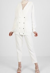 Witte dubbelgeknoopte jas met drukknopen en geribbelde manchetten, gecombineerd met bijpassende taps toelopende broek. Lichtgewicht stof met een zachte textuur.