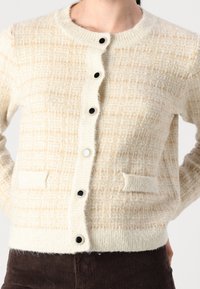 Svetr z vlněné směsi v krémové barvě s strukturovaným kostkovaným vzorem, s kulatým výstřihem, pěti černými knoflíky a dvěma předními kapsami.