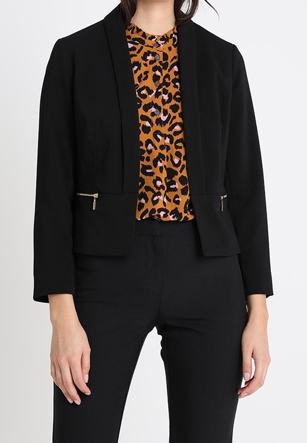 Černý zkrácený blejzr s přizpůsobeným střihem, s kapsami na zip. Nosený přes oranžový top s leopardím vzorem. Hladká tkanina, strukturovaný design.
