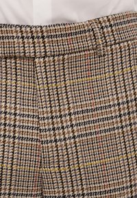 Pantalons en mélange de laine avec un motif à carreaux beige, marron et noir, ornés de fines lignes jaunes et roses, avec une taille ajustée.