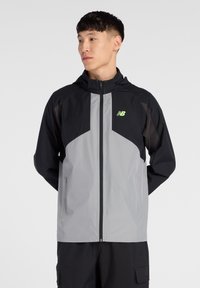 Lichte, gevoerde jas met capuchon in zwart en grijs. Voorzien van een ritssluiting aan de voorkant, gepaneeld ontwerp en reflecterend logo op de borst. Gladde textuur.
