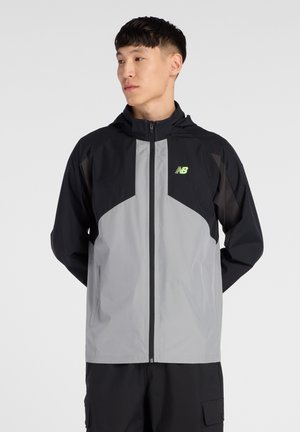 Lightweight, hooded jacket in black and gray. Features a zip front, paneled design, and reflective logo on the chest. Smooth texture.