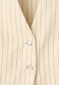 Tissu beige à fines rayures avec un motif discret en chevrons, présentant deux boutons argentés gravés qui ferment le devant d'un vêtement.