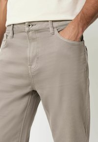 Meeste beežid püksid, mis on valmistatud siledast kangast, on varustatud eesmise taskuga, vöötagumistega ja metallnupuga kinnitusega. Kohandatud sobivus koos õmbluste detailidega.