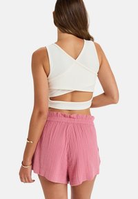 Vit ribbad crop top med V-format rygg, kombinerad med texturerade rosa shorts som har en volangdetalj på midjan och utsvängd nederkant.
