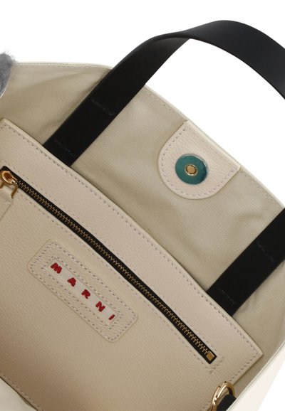 Borsa in pelle beige con manico nero, zip dorata e chiusura a scatto verde. L'interno presenta un'etichetta con logo cucita e una texture liscia.