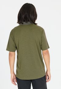 Mörkgrön kortärmad skjorta i mjukt tyg, med enkel, avslappnad passform och rundad nederkant, visad bakifrån.